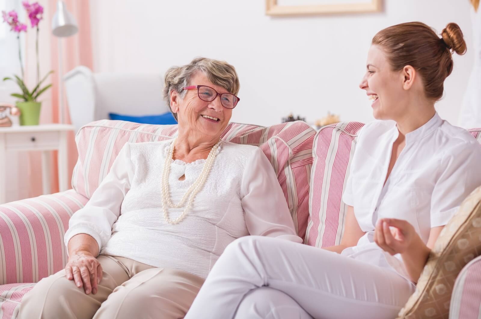 an adult child and a senior sit on a couch chatting